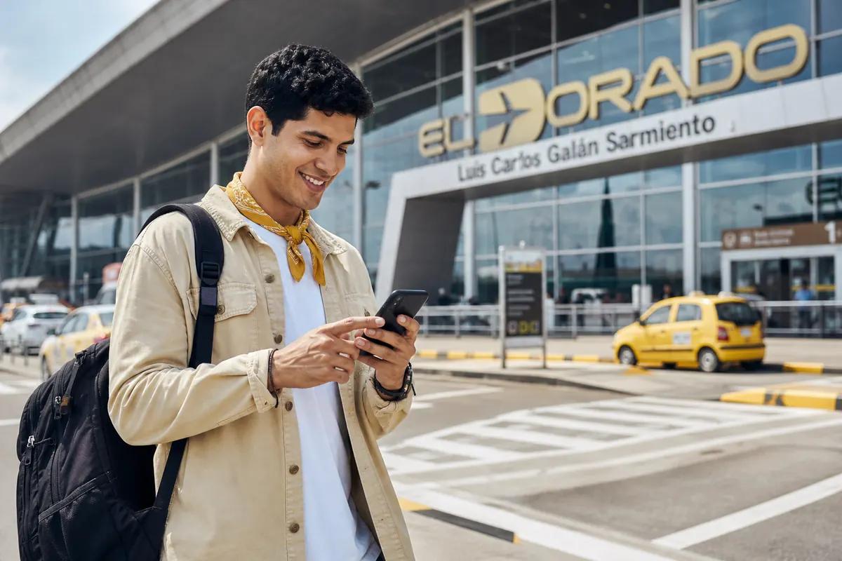 Backpacker checking his phone outside El Dorado airport with yellow taxis in the background