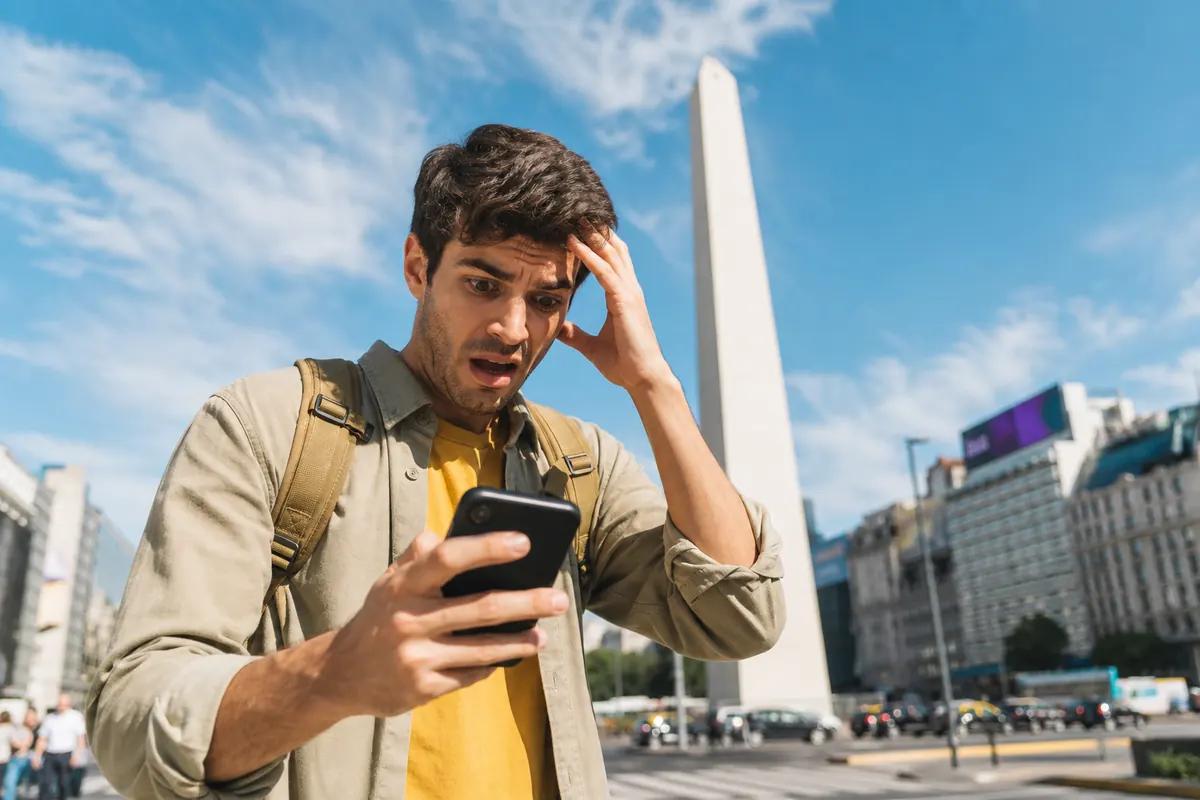 Dismayed traveler clutching his hair while staring at his phone in front of a sunlit obelisk