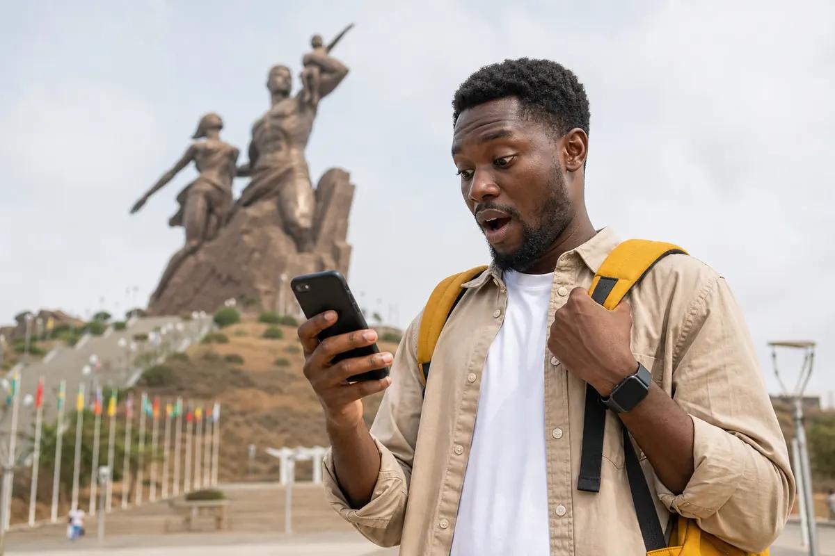 Traveler open-mouthed at his phone, a bronze monument and a row of flags rising behind him