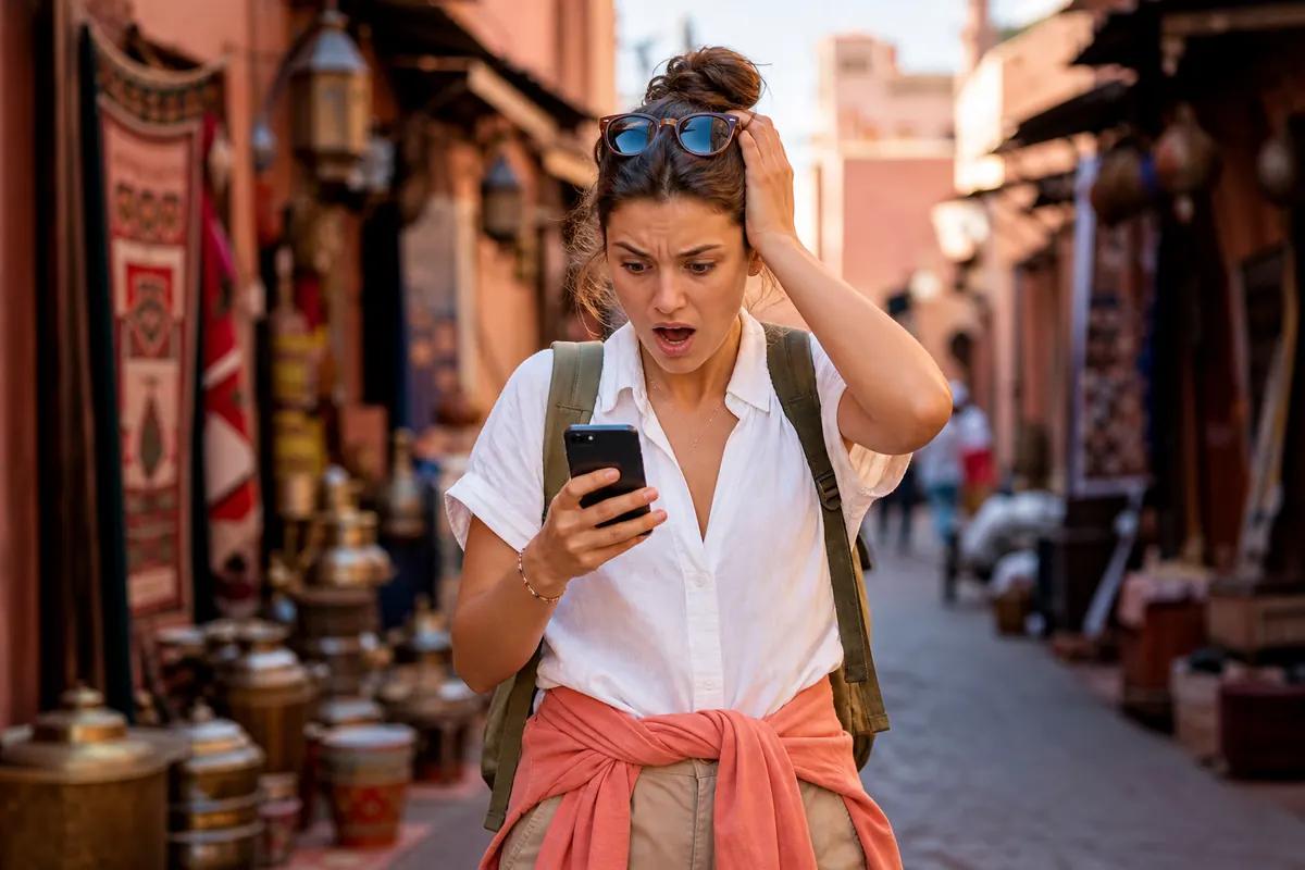 Shocked traveler staring at her phone in a souk alley lined with carpets and lanterns