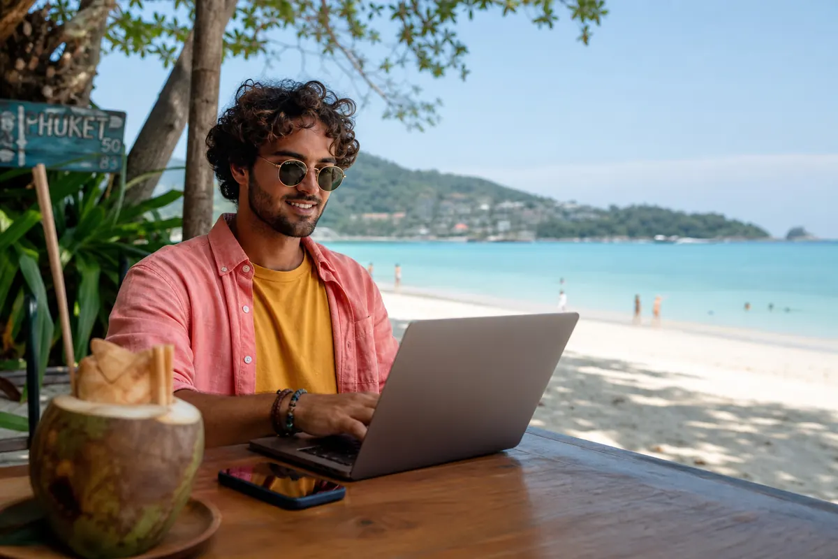 Traveler working on a laptop via mobile hotspot on a Phuket beach.